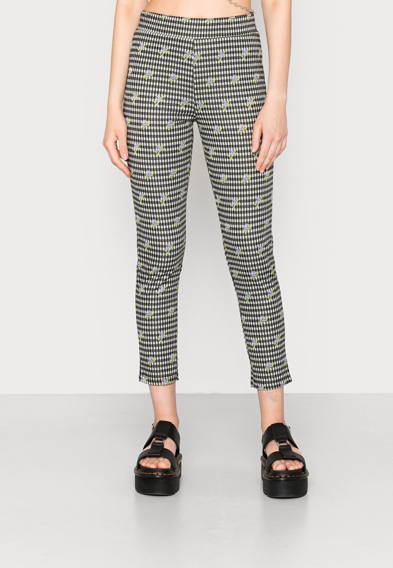 Pantalon style legging à motif à carreaux noir et blanc avec de petites fleurs violettes, porté avec des sandales à plateforme noires.