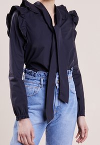 Blusa blu navy con spalle voluminose e scollatura annodata, abbinata a jeans in denim azzurro chiaro a vita alta con vita arricciata.