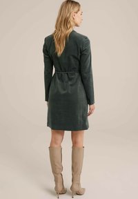 Rochie verde, cu mânecă lungă, cu talie ajustată și funda la spate. Țesătură fină, până la genunchi, asortată cu cizme bej până la genunchi.