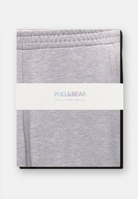 Harmaat juoksuhousut mustalla vyötäröosalla ja tarralla. Pehmeä kangas, taiteltu siististi, valkoisella brändätyllä vyöllä, jossa on "PULL&BEAR" ja slogan.
