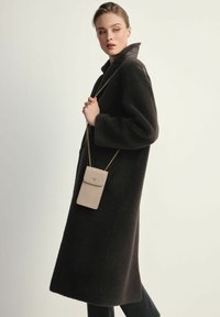 Czarny, teksturowany wełniany płaszcz z wysokim kołnierzem i oversize'owym krojem; zestawiony z jasnobeżową, teksturowaną torebką na łańcuszku.