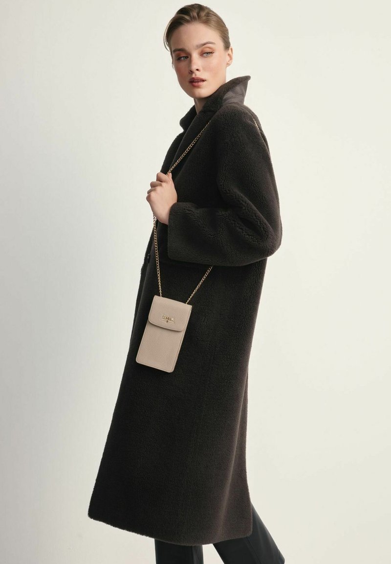 Czarny, teksturowany wełniany płaszcz z wysokim kołnierzem i oversize'owym krojem; zestawiony z jasnobeżową, teksturowaną torebką na łańcuszku.