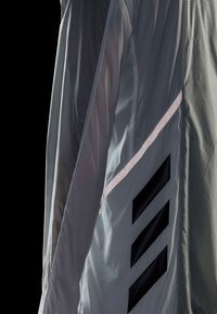 Gros plan d’un tissu gris avec trois larges bandes diagonales noires et une bande argentée réfléchissante sur un fond texturé.
