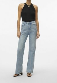 Czarny top na halter z teksturowanym splotem, w połączeniu z jasnoniebieskimi spodniami typu high-waisted w prostym kroju i czarnymi sandałami na obcasie.