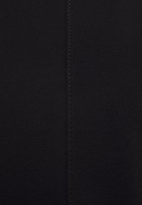 Svart tyg med en slät textur. Har en central söm med kontrasterande zick-zack-sömnad längs ena sidan.