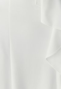 White fabric with a soft, layered ruffle detail on the right edge, showing texture and smooth drape.