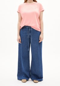 Ljusrosa t-shirt med uppvikt ärm, kombinerad med vida blåjeans i denim med dragsko i midjan och slät yta.