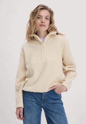 Crème-kleurige fleece pullover met een halve ritssluiting aan de voorkant, een iets verkorte snit en lange mouwen. Heeft een gladde textuur en geen patronen.
