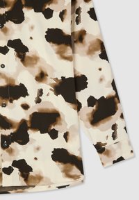 Camicia a maniche lunghe con fondo crema che presenta un motivo astratto in nero e marrone. Realizzata in tessuto morbido e liscio; chiusura con bottoni davanti.