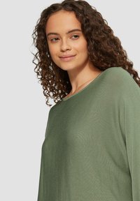 Grüner Strickoberteil mit weitem Ausschnitt und gerippter Textur, mit einem leicht lockeren Schnitt und langen Ärmeln.