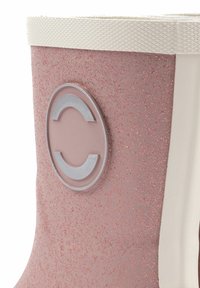 Botín de tobillo rosa con purpurina y un parche redondo de logo gris. Presenta una banda texturizada blanca en la parte superior y un acabado liso similar al caucho.