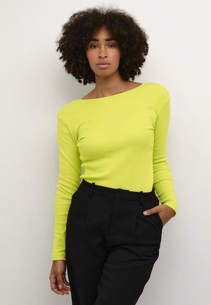 Dlouhý rukáv v jasné neonově žluté, vyrobený z žebrované látky, s off-shoulder výstřihem, kombinovaný s černými kalhotami s vysokým pasem.