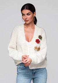 Vit stickad cardigan med djup V-ringning och broderade blommor i rött, beige och olivgrönt. Texturerat tyg och överdimensionerade ärmar.