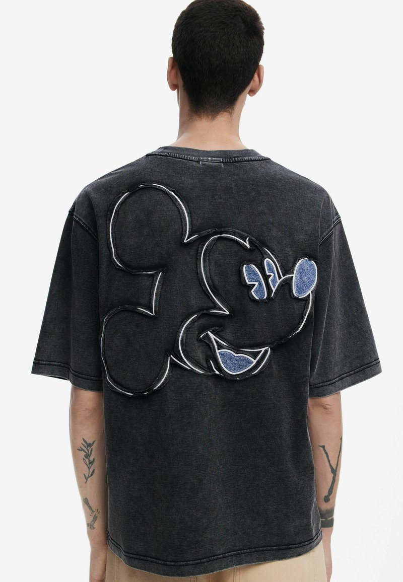 Camiseta de gran tamaño en gris oscuro con un gran diseño de Mickey Mouse en la parte posterior, contorneado con costuras blancas y con acentos azules en los ojos.