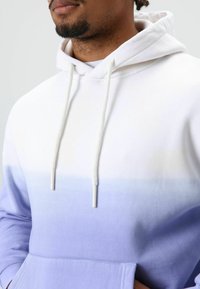 Kapuzenpullover mit Farbverlauf von Weiß zu Helllila, gefertigt aus weichem Stoff mit Kordelzug und einer Vordertasche.