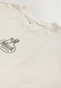 T-shirt en coton écru avec un logo Mack Trucks noir imprimé, représentant un bouledogue à l'intérieur d'un ovale, sur le côté gauche de la poitrine.