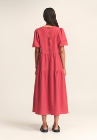 Robe midi a più strati di colore rosa con maniche a palloncino, bottoni sul retro e una silhouette fluida. Realizzata in un tessuto leggero con una superficie liscia.