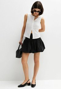 Top bianco senza maniche con tessuto texture e chiusura a bottoni, abbinato a una gonna mini nera svasata e scarpe con tacco blocco nere.