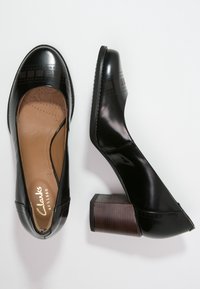 Escarpins en cuir noir avec bout arrondi, bande texturée décorative, talon bloc à fini imitation bois, et semelle intérieure beige avec logo.