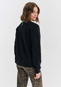 Černá mikina se zaobleným výstřihem a žebrovanými manžetami, kombinovaná s kalhotami s leopardím potiskem. Obsahuje barevný akcent na zadní straně výstřihu.