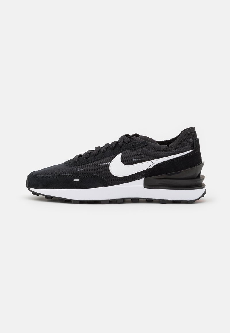 Fekete sportcipők velúr és szövet felsőrésszel, fehér Nike logóval, fekete gumitalppal és párnázott sarokkal a kényelem érdekében.