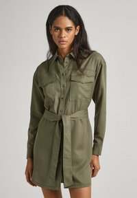 Abito camicia verde oliva con bottoni frontali, due tasche sul petto e una cintura in tessuto. Maniche lunghe e vestibilità su misura. Texture liscia.