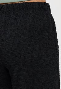 Sorte, teksturerte joggebukser med elastisk midje og mykt, fleece-liknende materiale. Fokuserer på komfort og uformell bekledning.