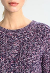 Maglione lavorato a maglia con colletto rotondo, caratterizzato da un motivo testurizzato in filato blu navy, rosa e bianco. Il tessuto appare accogliente e di peso medio.