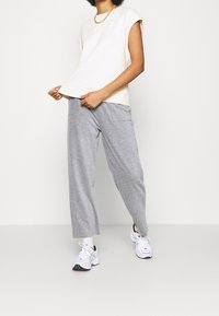 Top corto de manga corta color crema combinado con pantalones de chándal grises sueltos. El atuendo presenta un ajuste casual y una tela texturizada, complementado con zapatillas blancas.