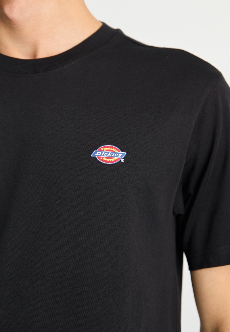 Black cotton t-shirt with short sleeves and a crew neck; features a small, colorful "Dickies" logo on the upper left chest.