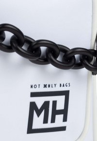 Bolso blanco con un acabado texturizado, que presenta una prominente correa de cadena negra y una marca negra: "MH" y "NOT ONLY BAGS."