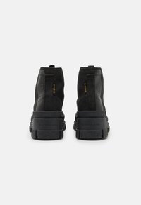Stivaletti alla caviglia in suede nero con suola in gomma testurizzata. Dettagli notevoli includono un marchio impresso e una linguetta sul tallone per una facile calzata.