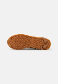 Semelle de chaussure en caoutchouc marron avec des grips circulaires et des motifs rainurés, avec le logo "Tommy Hilfiger" au centre.