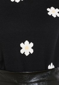 Suéter de punto negro con patrones de flores blancas, con una textura suave y acentos en color beige en el centro. Incluye un cinturón brillante negro en la cintura.