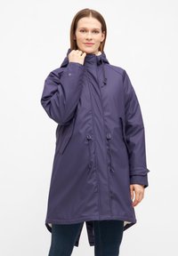 Lila, vattentät ytterjacka med huva, dragsnören och sidofickor; har en lös passform och längre bakstycke.