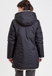 Abrigo acolchado negro con capucha, con un forro de felpa blanca en el dobladillo y en los puños, textura suave y silueta larga.