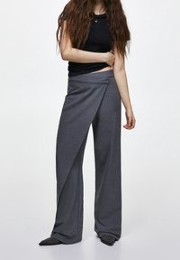 Pantalon gris à jambes larges avec un design enveloppant et une texture lisse. Porté avec un haut noir cintré, présentant un col bénitier.