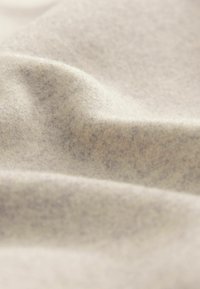 Tejido de lana suave color beige claro con una textura fina y pliegues suaves que crean sombras y reflejos sutiles.