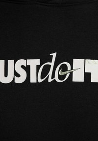 Tessuto nero con grandi lettere bianche che scrivono "JUST do IT", caratterizzato da un piccolo swoosh Nike verde. Texture liscia, design casual.
