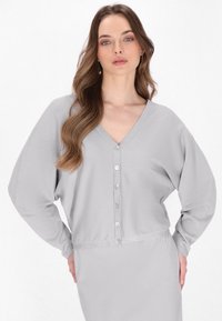 Lichtgrijze lange mouwen cardigan met V-hals, voorzien van zes knoopsluitingen en een zachte textuur. Losse pasvorm en licht cropped ontwerp.