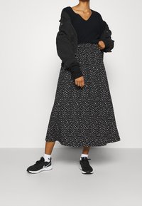 Maglione nero a scollo a V, giacca bomber nera oversize, gonna maxi con stampa floreale in bianco e nero e scarpe sportive nere con dettagli bianchi.