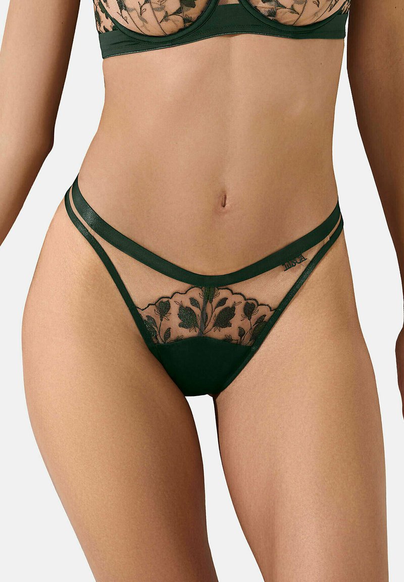 String vert en dentelle avec broderie florale, présentant des panneaux en maille transparente et des doubles fines bretelles. Partie inférieure en tissu lisse.