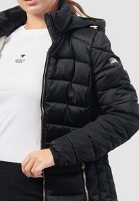 Giacca a vento nera con zip frontale, cappuccio e design trapuntato. Caratterizzata da polsini elasticizzati e una patch con logo sulla manica.