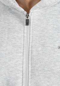 Grauer Reißverschluss-Hoodie aus weichem Material, mit einem silbernen Reißverschluss, kontrastierenden Nähten und einem kleinen Akzentdetail auf der Brust.