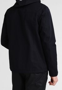 Marinblå vattenavvisande jacka med huva, som har en slät textur och en minimalistisk design. Inkluderar diskret sömnad och rak skärning.