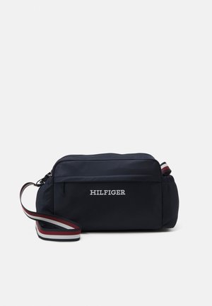 Sac bandoulière rectangulaire bleu marine avec poche zippée à l'avant, texte "HILFIGER" et bandoulière réglable avec des rayures rouges, blanches et bleu marine.