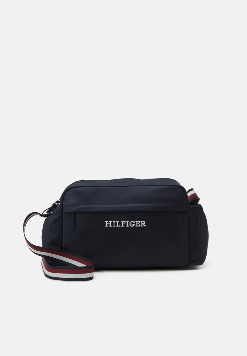 Navy blue rectangular crossbody bag with front zipper pocket, "HILFIGER" text, and adjustable strap with red, white, and navy stripes.