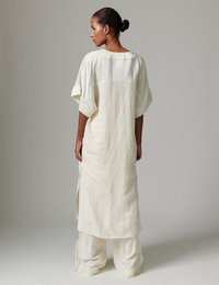 Μακρύ, άνετο φόρεμα από απαλό λευκό ύφασμα με στρογγυλή λαιμόκοψη και κοντά μανίκια· πλαϊνές σχισμές και ραφές σε αντίθετο χρώμα. Συνδυάζεται με φαρδιά λευκά παντελόνια.