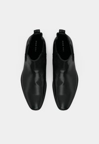 Ein Paar schwarze Leder Chelsea-Boots mit eckiger Zehenform, von oben auf einem weißen Hintergrund betrachtet.