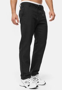Black drawstring pants made of a textured fabric, featuring side pockets and a tapered design, paired with white and black sneakers.